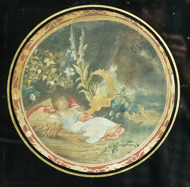 An early 19th century framed circular silk worked embroidery, by M Bovi after a R Westhall painting ‘The gleaners child’, Verre Eglomise mounted. The embroidery of a sleeping child lying on a cushion under a tree surroun
